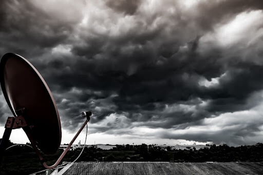 Satellite dish facing to dark storm cloud